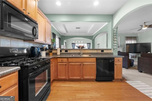 kitchen with a peninsula, a sink, open floor plan, black appliances, and dark countertops