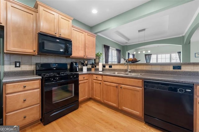 kitchen featuring light wood-style floors, dark countertops, a sink, black appliances, and backsplash