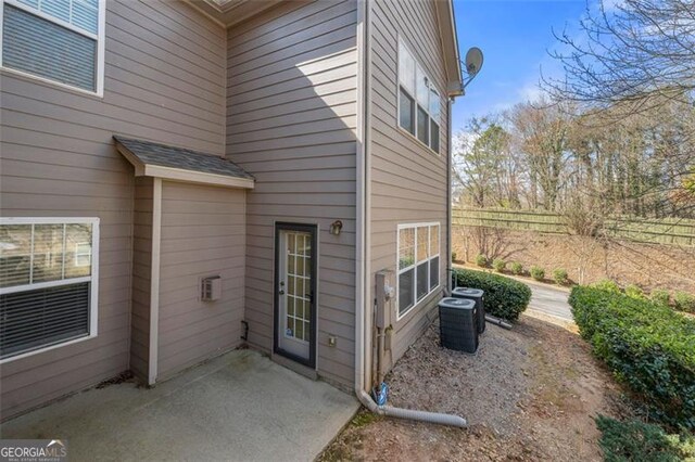 entrance to property featuring roof with shingles, fence, central AC, and a patio