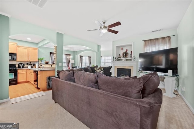 living room with ceiling fan, baseboards, a glass covered fireplace, and light colored carpet