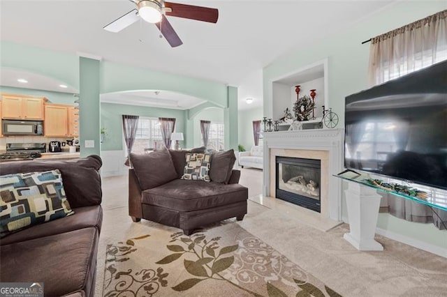 living room featuring light carpet, ceiling fan, a premium fireplace, and arched walkways