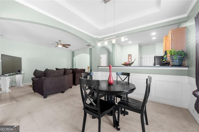 dining area featuring a tray ceiling, light carpet, ceiling fan, and arched walkways