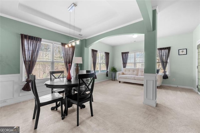 dining area featuring light carpet, arched walkways, a raised ceiling, and wainscoting