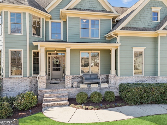 doorway to property featuring brick siding, roof with shingles, and a porch