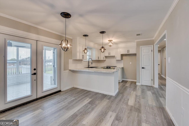 kitchen with white cabinets, ornamental molding, a peninsula, light countertops, and a sink