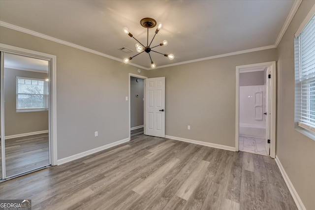 unfurnished bedroom with baseboards, ornamental molding, light wood finished floors, ensuite bath, and an inviting chandelier