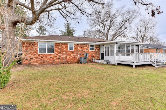 back of property with a sunroom, a deck, a lawn, and brick siding