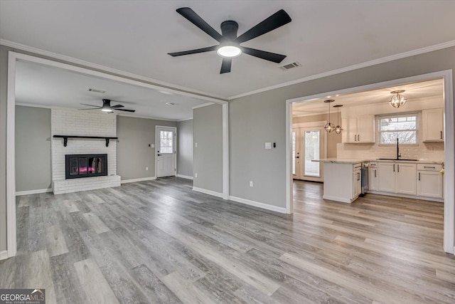 unfurnished living room featuring crown molding, visible vents, a sink, and light wood finished floors