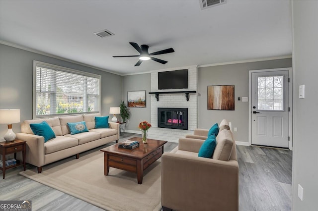 living area with light wood-style flooring, a fireplace, ornamental molding, and visible vents