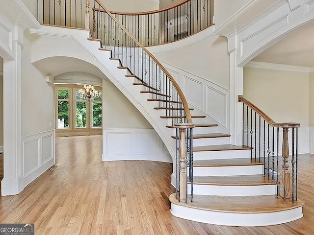 stairway with a notable chandelier, crown molding, a decorative wall, and wood finished floors