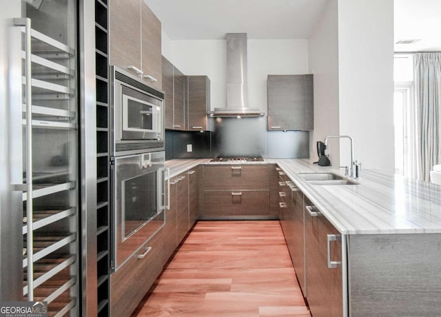 kitchen featuring wall chimney exhaust hood, modern cabinets, appliances with stainless steel finishes, light stone countertops, and a sink