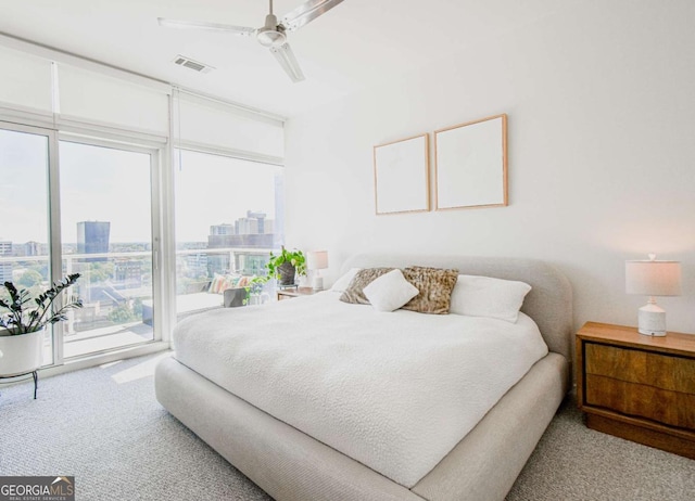 carpeted bedroom with visible vents, ceiling fan, access to exterior, expansive windows, and a city view