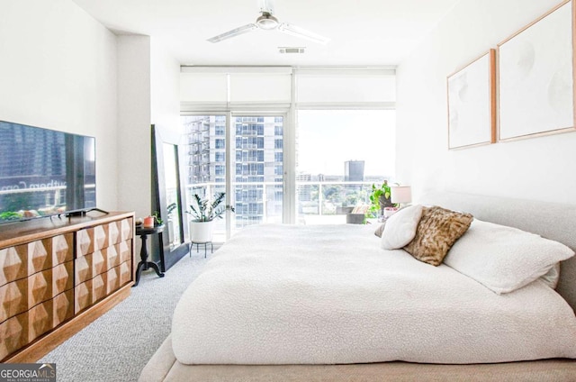 bedroom featuring light carpet, visible vents, a ceiling fan, expansive windows, and a view of city