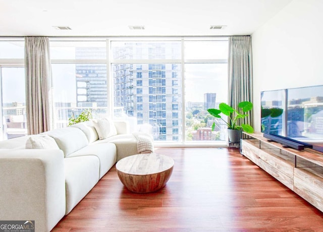 living room with a healthy amount of sunlight, floor to ceiling windows, visible vents, and wood finished floors