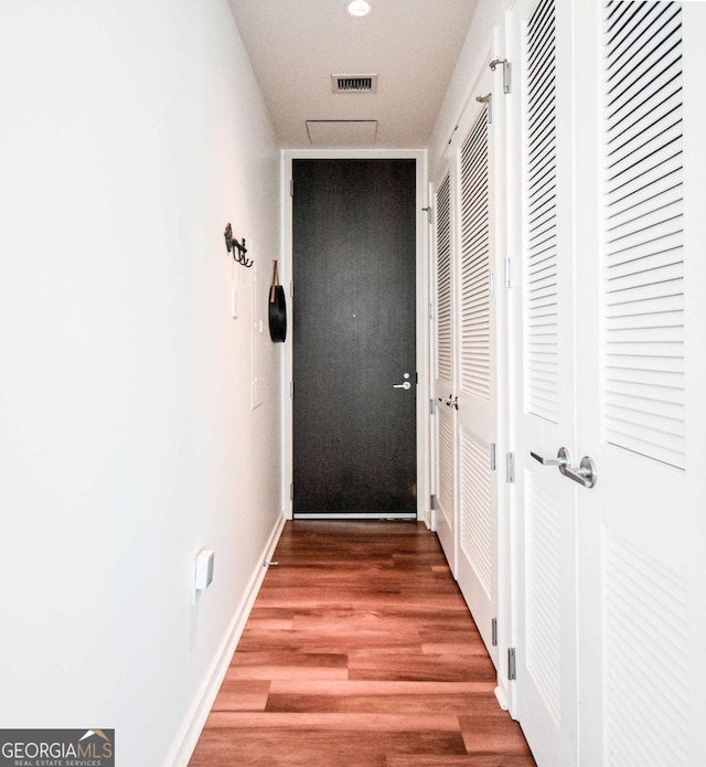 hall featuring visible vents, baseboards, and wood finished floors