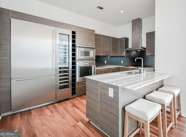 kitchen with a breakfast bar area, visible vents, modern cabinets, built in appliances, and wall chimney exhaust hood