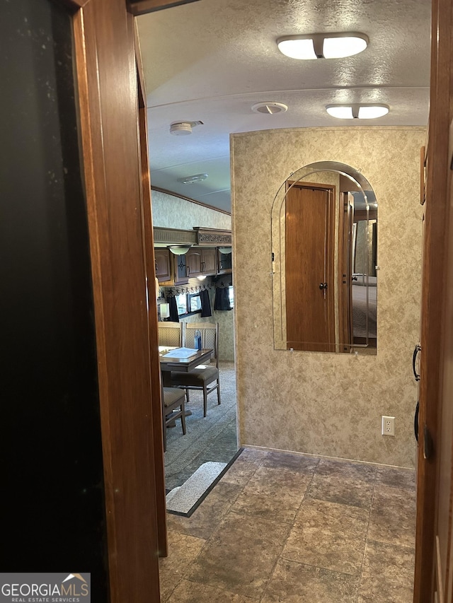 hallway with wallpapered walls, crown molding, arched walkways, and a textured ceiling