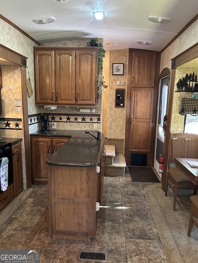 kitchen with a center island, dark countertops, visible vents, wall oven, and ornamental molding