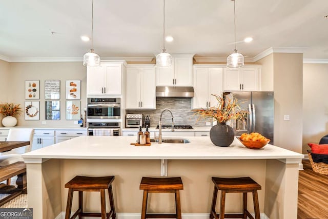 kitchen featuring light countertops, appliances with stainless steel finishes, a kitchen island with sink, and under cabinet range hood