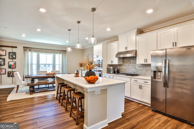 kitchen featuring under cabinet range hood, stainless steel appliances, a kitchen island, hanging light fixtures, and light countertops