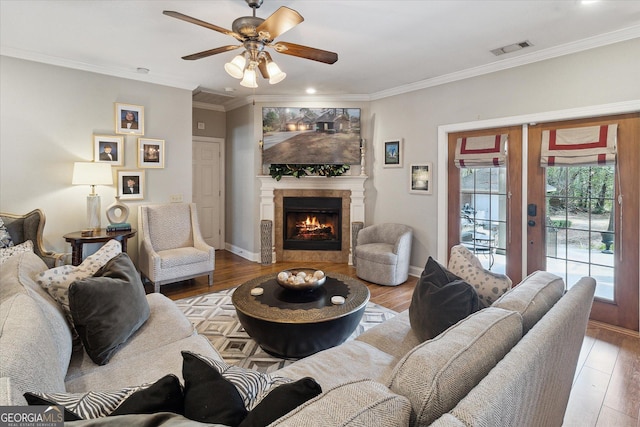 living room with a warm lit fireplace, visible vents, baseboards, ornamental molding, and light wood-type flooring