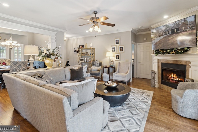 living area featuring recessed lighting, ceiling fan with notable chandelier, wood finished floors, ornamental molding, and a tiled fireplace