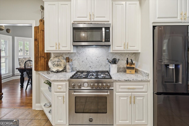 kitchen featuring white cabinets, tasteful backsplash, light stone counters, and stainless steel appliances