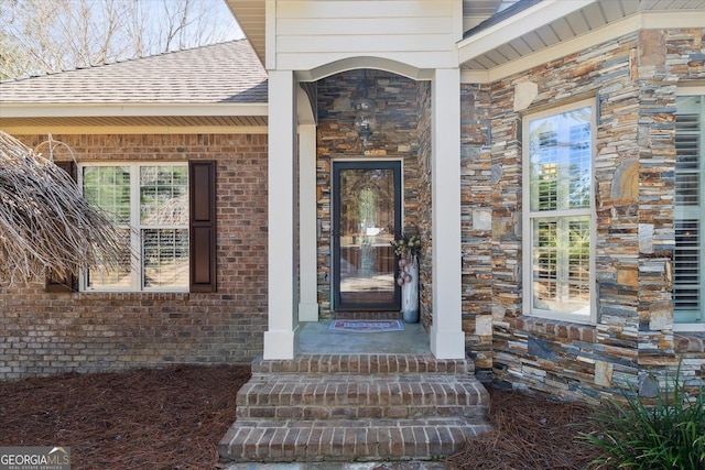 view of exterior entry featuring brick siding, stone siding, and roof with shingles