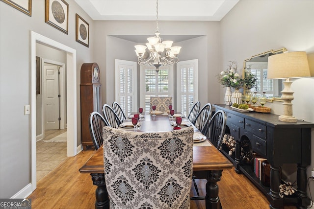 dining space with light wood-type flooring, baseboards, a chandelier, and a tray ceiling