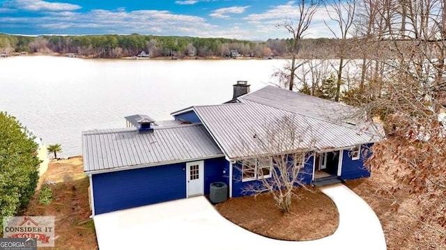 view of front facade featuring cooling unit, a water view, metal roof, and a chimney