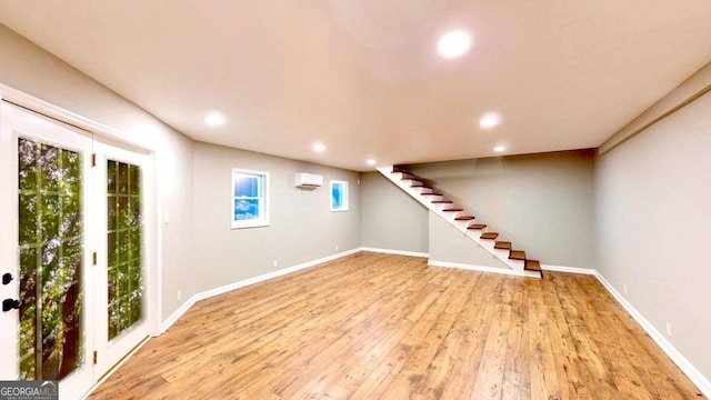 below grade area with baseboards, light wood-style flooring, stairway, an AC wall unit, and recessed lighting