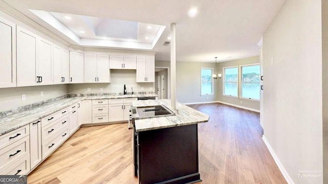 kitchen with light wood finished floors, white cabinets, light stone countertops, pendant lighting, and a sink