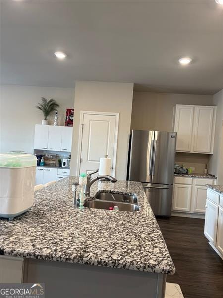 kitchen featuring an island with sink, light stone countertops, a sink, and freestanding refrigerator