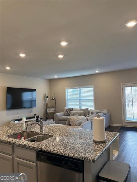 kitchen with a kitchen island with sink, a sink, open floor plan, stainless steel dishwasher, and light stone countertops