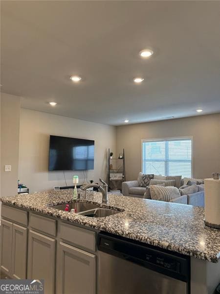 kitchen featuring a sink, stone countertops, open floor plan, and dishwasher