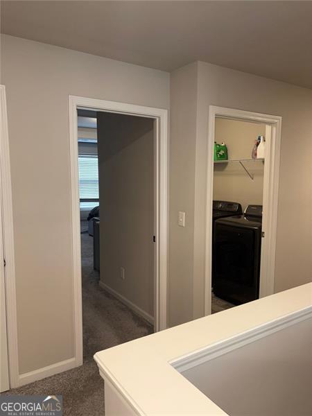 corridor featuring baseboards, dark carpet, and independent washer and dryer