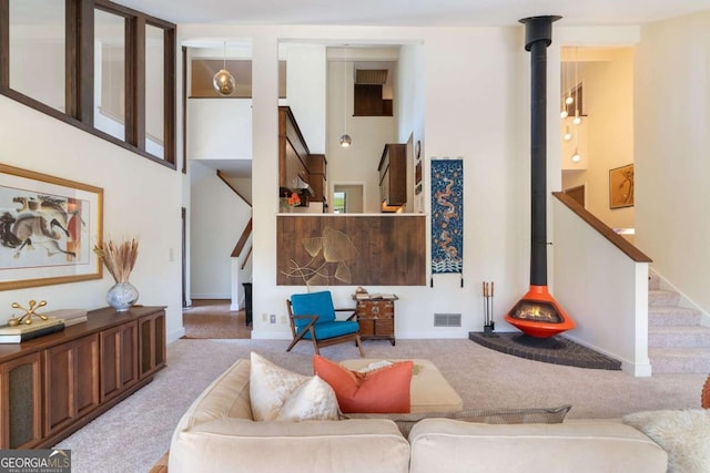 living room with a wood stove, stairs, and light carpet