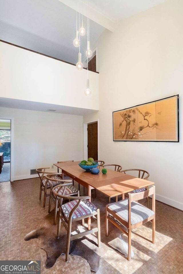 dining space featuring a towering ceiling, baseboards, and beamed ceiling