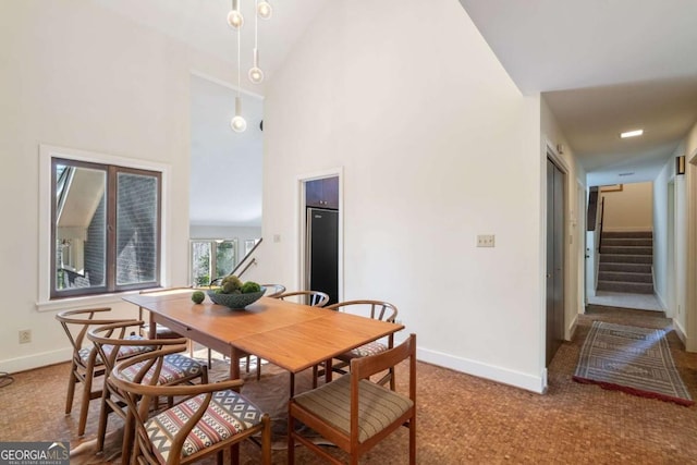 carpeted dining area featuring high vaulted ceiling, stairway, and baseboards