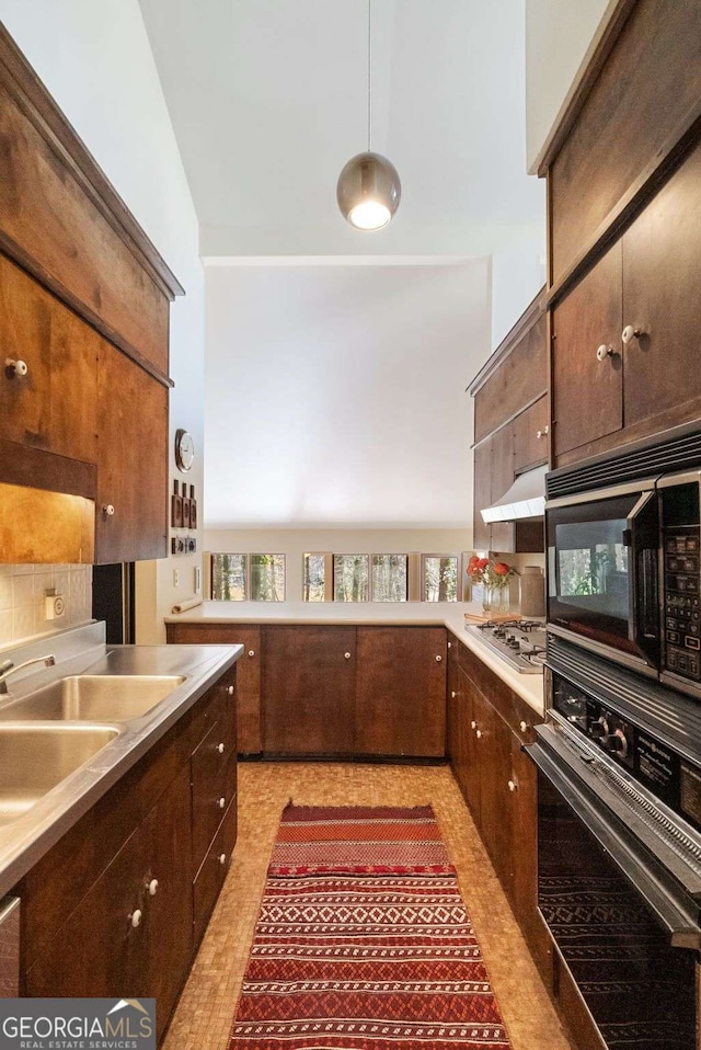 kitchen featuring light countertops, appliances with stainless steel finishes, a sink, dark brown cabinets, and under cabinet range hood