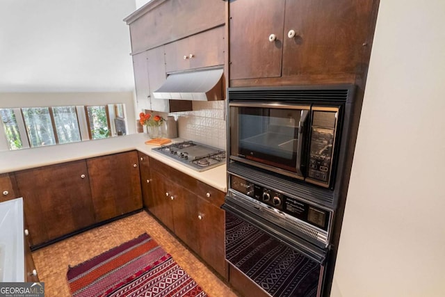 kitchen with light countertops, backsplash, dark brown cabinetry, under cabinet range hood, and black appliances