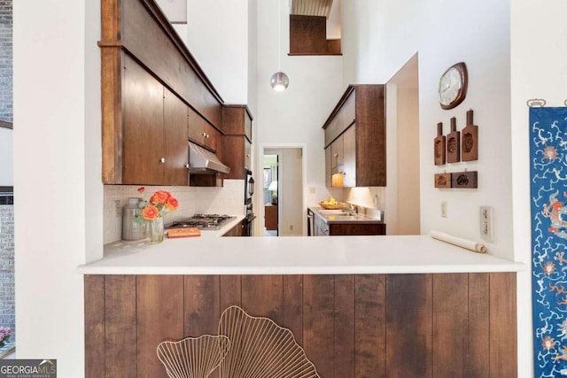 kitchen with light countertops, a peninsula, backsplash, and under cabinet range hood