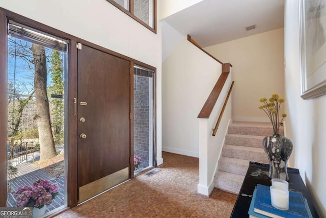 foyer entrance featuring stairway, baseboards, visible vents, and carpet flooring