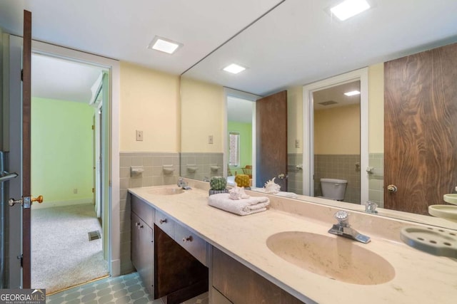 full bathroom with double vanity, a sink, toilet, and tile walls