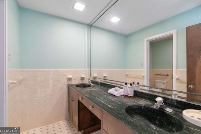 full bath featuring double vanity, tile walls, a sink, and wainscoting