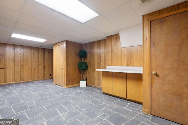 finished basement featuring a drop ceiling, wooden walls, and baseboards