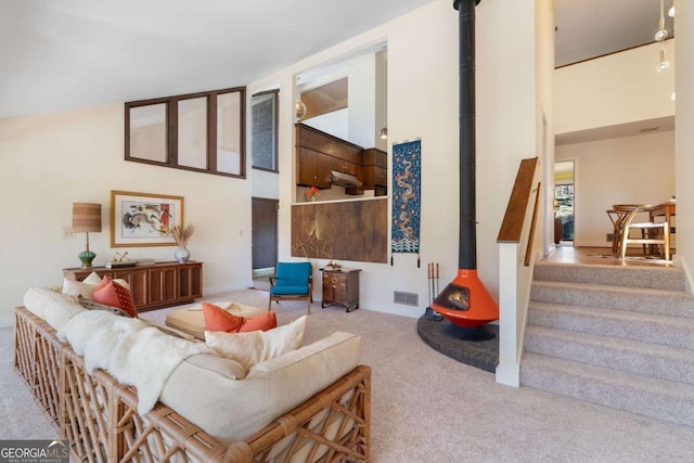 living room featuring visible vents, high vaulted ceiling, carpet flooring, and a wood stove