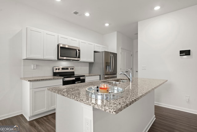 kitchen with appliances with stainless steel finishes, white cabinetry, a center island with sink, and light stone counters