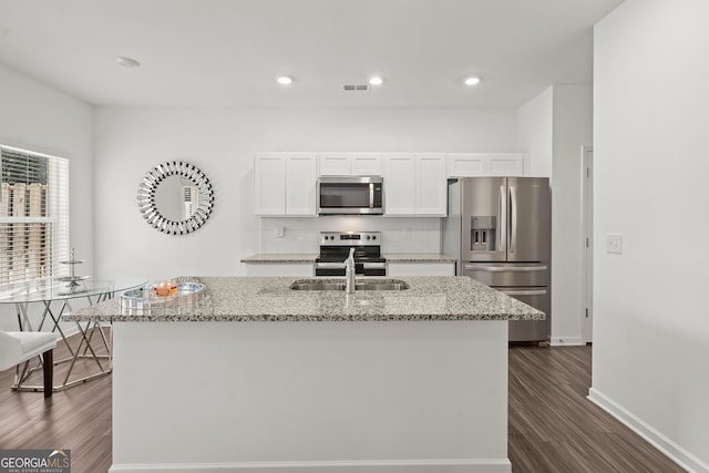 kitchen with light stone counters, stainless steel appliances, tasteful backsplash, white cabinets, and an island with sink