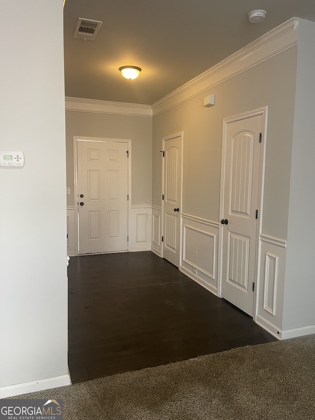 corridor featuring a decorative wall, a wainscoted wall, dark wood-type flooring, visible vents, and ornamental molding